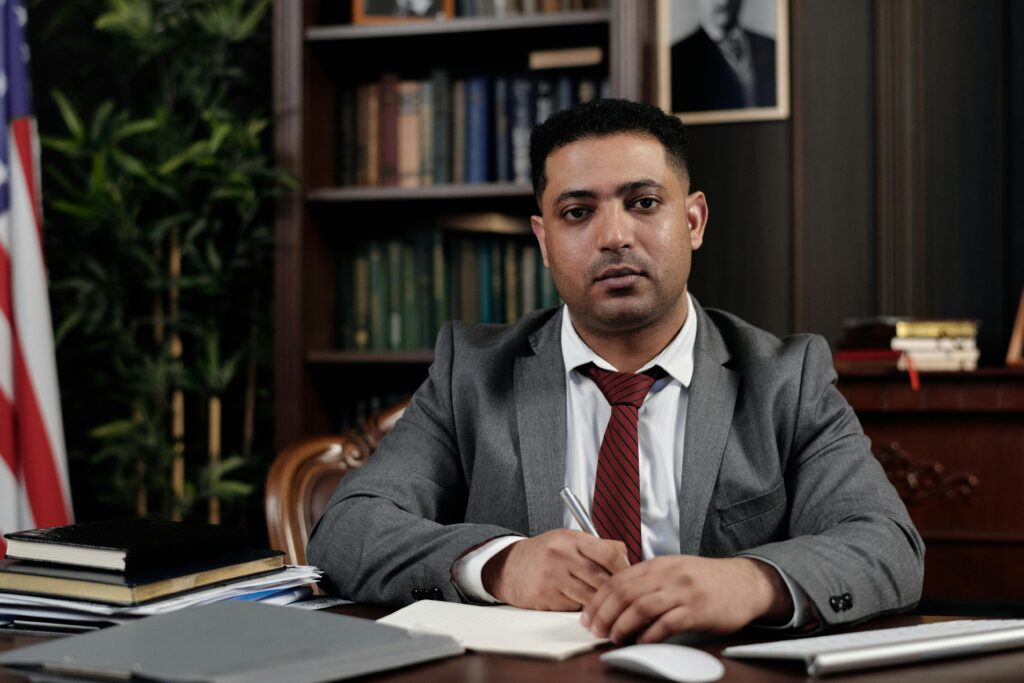 A serious businessman in a suit writing at his desk in a formal office setting.