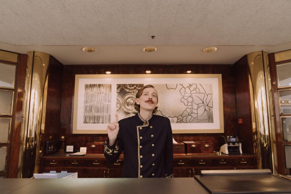 A luxury hotel receptionist in uniform stands behind the opulent front desk, ready to assist guests.